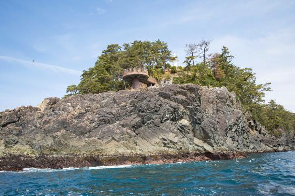 海から見た碁石埼灯台と碁石岬の展望台の写真