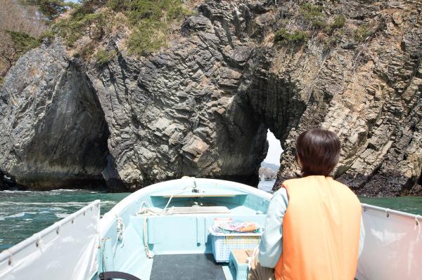 大きな岩に開いている穴を船に乗って潜り抜けようとしている女性の後姿の写真
